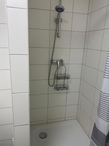 a shower with a hose in a white tiled bathroom at Fuchsbau Komfort Zimmer in Nordhausen