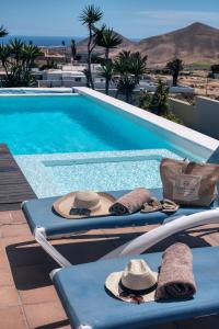 a swimming pool with two lounge chairs with hats on them at Villa El Erizo - Pool By Lanzarote Vacation Homes in Nazaret