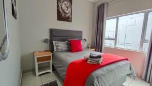 a bedroom with a bed with a red blanket and a window at Utopia Guest House in Alberton