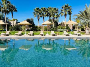 a pool with chairs and umbrellas and palm trees at Les Villas du Douar in Azib Oulad Lâdem