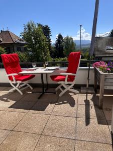 two red chairs and a table on a patio at Appartement 2 chambres avec balcon terrasse in Villars-sur-Glâne