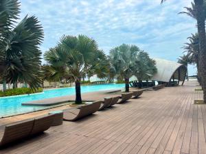 a row of benches next to a swimming pool with palm trees at D02 - Happy Beach Villas - No2 Căn hộ Z&Z Triple key - NovaWorld Ho tram in Binh Chau