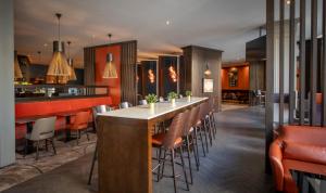 a restaurant with a long bar with orange chairs at Clayton Hotel, Leeds in Leeds