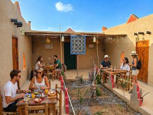 a group of people sitting at tables outside a house at Riad dar merzouga in Merzouga