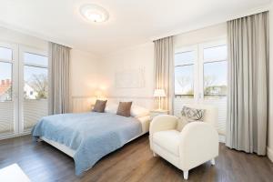 a bedroom with a bed and a chair and windows at Haus Vogelflug strandleev3 in Fehmarnsund