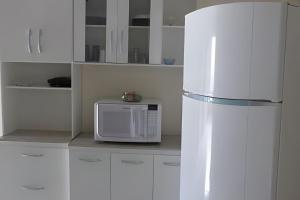 a white kitchen with a microwave and a refrigerator at Casa do Bruno, 600 mt do thermas in Olímpia