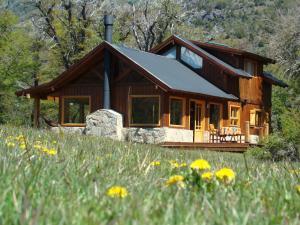 a log cabin in the woods with a field of flowers at Casa Lago Meliquina in Lago Meliquina
