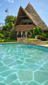a resort swimming pool with a thatch roof at Fasha House Malindi in Malindi