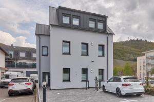a white building with two cars parked in a parking lot at Burgblick Apartment Weinlaub in Bernkastel-Kues