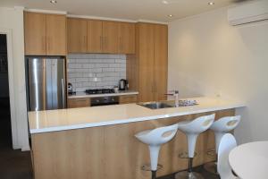 a kitchen with wooden cabinets and white stools at Matagouri Cottage - Lake Tekapo in Lake Tekapo