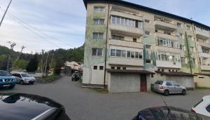 a tall building with cars parked in a parking lot at Montain apartament in Brezoi
