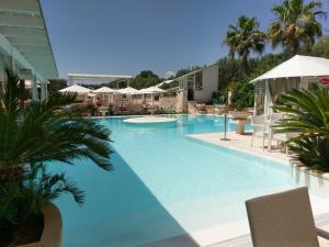 a large blue swimming pool with palm trees and umbrellas at Borgo Pascarosa in Ostuni