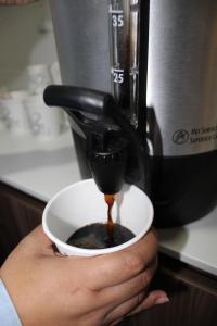 a person holding a cup of coffee with a coffee maker at Hi! Monterrey Aeropuerto in Monterrey