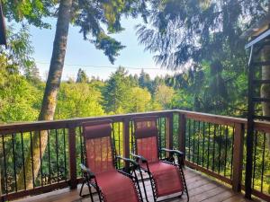 two chairs on a deck with a view of trees at Owl's Perch Treehouse in Sooke