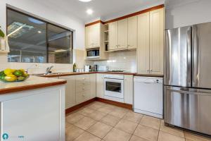 a kitchen with white cabinets and a stainless steel refrigerator at Beachside Largs Bay Pet Friendly 3 Bed Haven in Birkenhead
