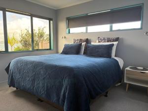 a bedroom with a blue bed with two windows at Beach Lane Apartment in Whangarei