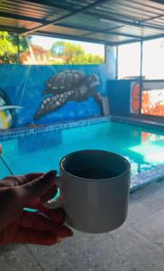 a person holding a cup in front of a swimming pool at Pousada Hotel Sol Nascente in Mafra