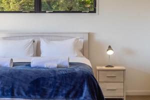 a bedroom with a bed with a blue blanket and a lamp at Hekerua Heights with Hot Tub and Seaviews in Oneroa