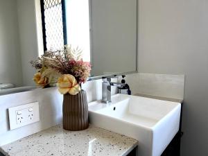 a bathroom with a white sink and a vase with flowers at 14A Convenient Ensuite Room in Coopers Plains in Brisbane +11 photos