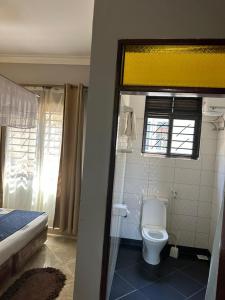 a bathroom with a toilet and a bed and a window at Aape Motel Kamuli in Kamuli