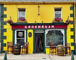 a yellow building with chairs in front of a store at Geoghegans Magpie Bar and B&B in Glin