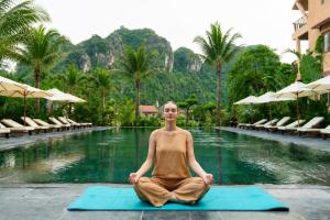 a woman sitting in a yoga pose in front of a pool at Aman Retreat Ninh Binh in Ninh Binh
