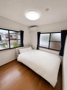 a bedroom with a white bed and two windows at Glad Kasuga in Kasugabaru