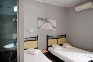 two beds in a room with a sink and a bathroom at Electra Hotel Piraeus in Piraeus