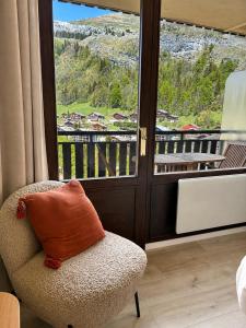 a chair with an orange pillow sitting in front of a window at Lodge Montëva - Le Chinaillon - Au pied des pistes in Le Grand-Bornand