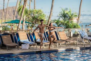 a man and a woman standing by a swimming pool at OUTRIGGER Waikiki Beach Resort in Honolulu