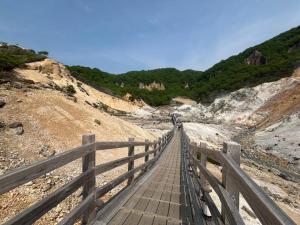 a wooden bridge on a beach with rocks and trees at Horomisou in Noboribetsu