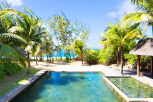 a swimming pool in front of a beach with palm trees at Beach Penthouse BELMARE in Belle Mare