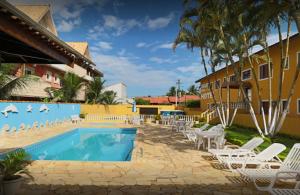 a swimming pool with white chairs and a resort at Hotel Xapuri in Peruíbe