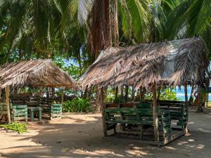 zwei Strohschirme und eine Bank mit Stühlen darunter in der Unterkunft Playa 506 Beachfront Hostel in Puerto Viejo