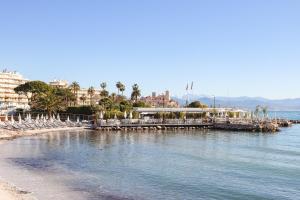 a beach with a pier and buildings and palm trees at Royal Antibes - Luxury Hotel, Résidence, Beach & Spa in Antibes