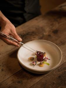 a person holding a pair of tongs over a plate of food at Naturhotel Lüsnerhof in Luson