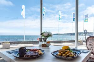 a table with two plates of food on a table with the ocean at The Queens Hotel in Penzance
