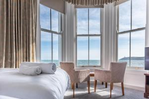 a bedroom with a bed and two chairs and windows at The Queens Hotel in Penzance