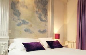 a bed with two purple pillows in front of a painting at Hostal Terán in Madrid