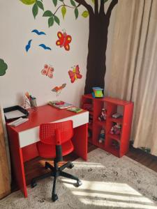 a red desk with a red chair and a tree on the wall at Artisan Center Apartment Peja in Peje +1 photo