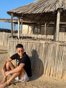 a man sitting in the sand in front of a wooden fence at Hotel Cabo Royal in Cabo de la Vela