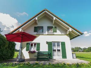 ein kleines weißes Haus mit einem roten Sonnenschirm und einer Bank in der Unterkunft Alluring Holiday Home in Ubersee with Whirlpool in Übersee + 32 Fotos