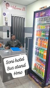 a man sitting at a desk in front of a soft drink cooler at Soni Hotel in Hanumāngarh