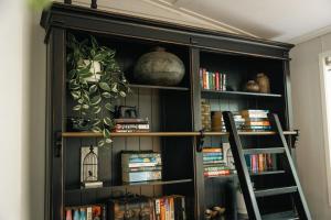 a black book shelf with books and a bird cage at The Foxman Cottage in Broke