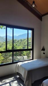 a bedroom with a large window with a view at Casa Chalé dos Pinhas - Chalé Romântico e Aconchegante - Hidromassagem - Lareira - Vista da Montanha - Próximo a Campos do Jordão in Santo Antônio do Pinhal