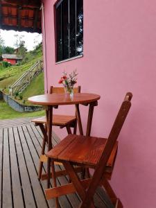 a wooden table and chair on a deck with a pink wall at Chalé Sonho Diniz 1 in Monte Verde