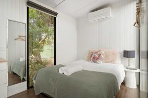 a white bedroom with a bed and a large window at Halls Haven Tiny House 1 by Tiny Away in Halls Gap