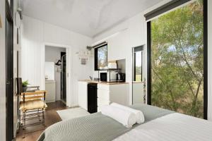 a bedroom with a bed and a kitchen with a large window at Halls Haven Tiny House 1 by Tiny Away in Halls Gap