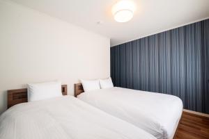 two beds in a bedroom with white sheets and blue curtains at Villa Shigin in Nakafurano