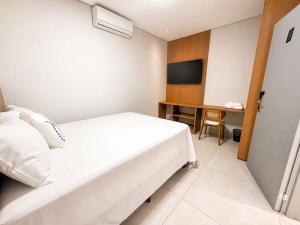 a hotel room with a white bed and a television at Hotel El Shaddai in Pontes e Lacerda